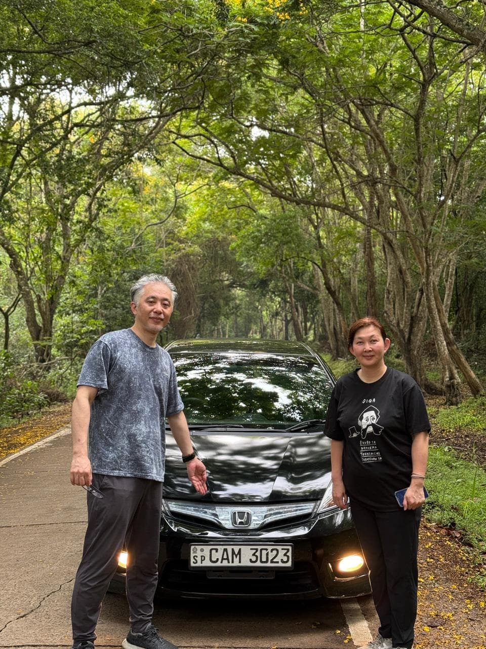 Travellers beside their car on a tree-canopied jungle road