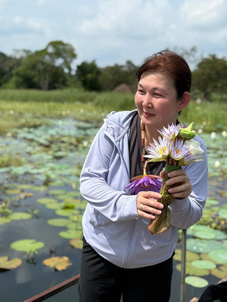 A traveller holding freshly picked lotus flowers on a boat trip through a lily pond