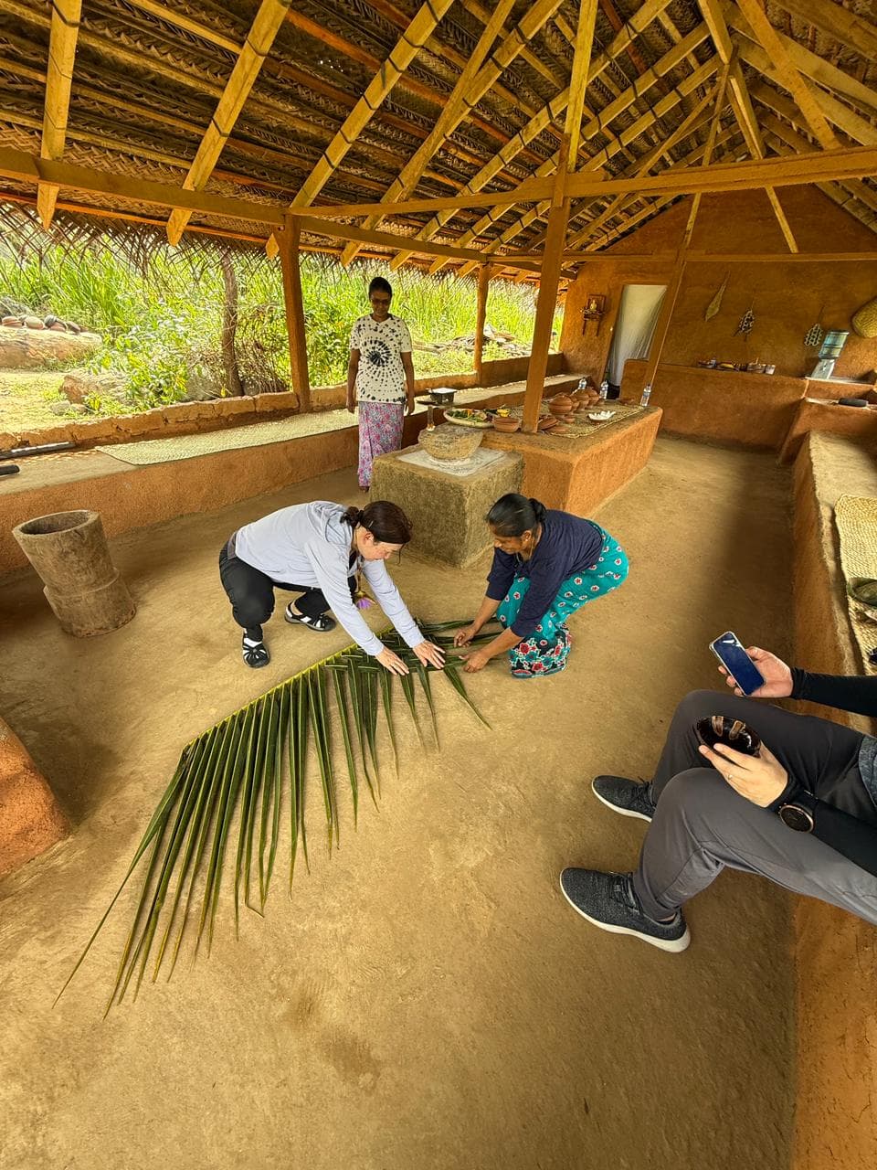 A traveller learning traditional palm-leaf mat weaving with a local host